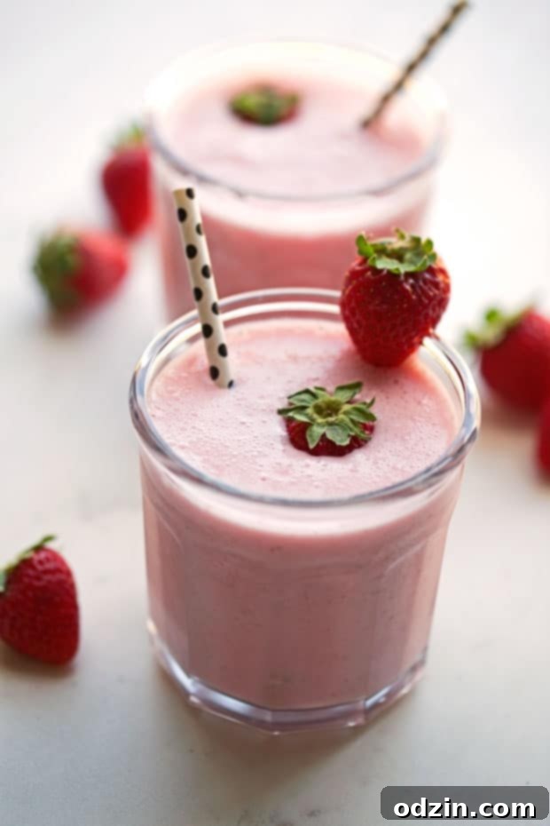 Homemade Strawberry Rose Lassi, vibrant pink in color, garnished with a fresh strawberry on the rim of the glass. A creamy, refreshing yogurt drink, perfect for a quick treat or Valentine's Day celebration.