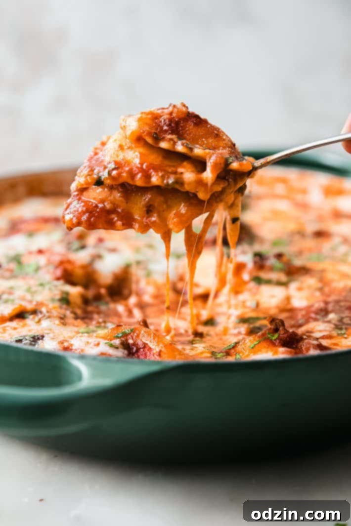 Cheater's Skillet Ravioli Lasagna 3 A fork lifting a piece of perfectly cooked ravioli lasagna from a cast iron skillet, showcasing the cheesy layers