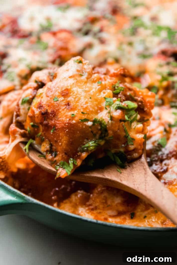 Cheater's Skillet Ravioli Lasagna 5 Close-up of a portion of ravioli skillet lasagna being scooped with a spoon, showing gooey cheese and rich meat sauce