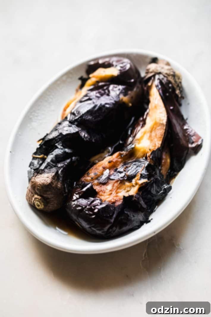 A large eggplant roasting over an open gas flame on a stove top, charring beautifully.