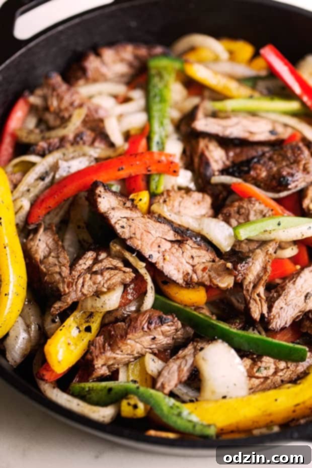 Sizzling Steak Fajita Perfection 2 cast iron pan with sliced steak, peppers, and onions