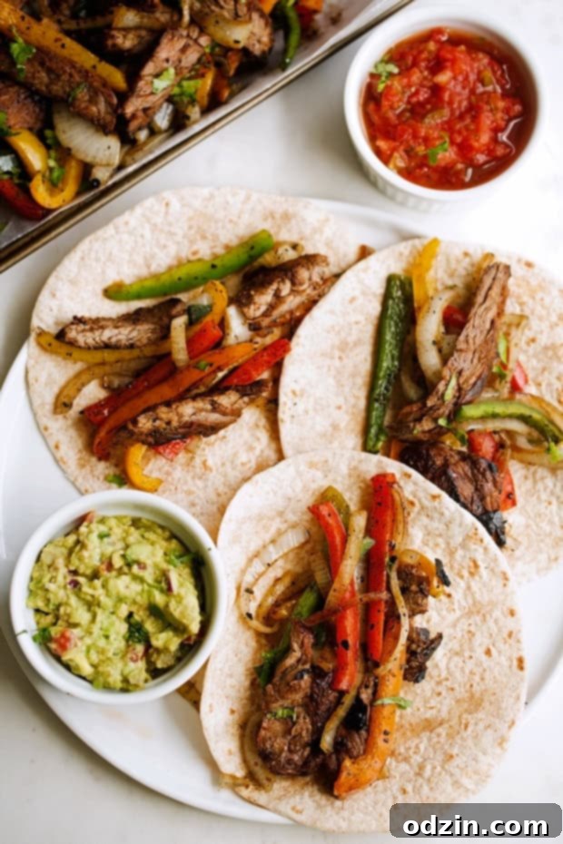 Sizzling Steak Fajita Perfection 3 beef fajitas with peppers and onions on tortillas with bowls of guacamole and salsa