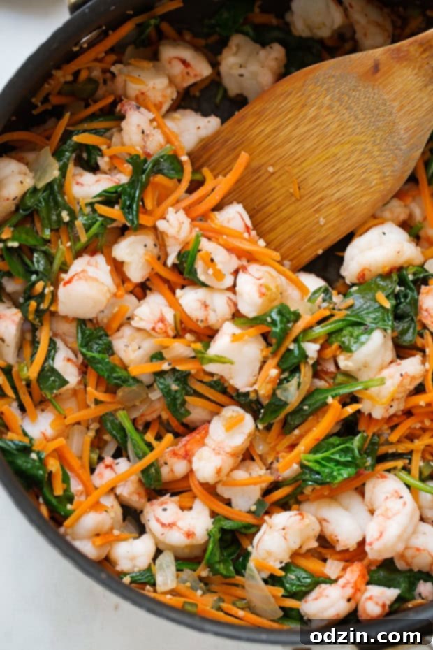 Shrimp Enchiladas with Creamy Poblano Sauce - Simple and delicious shrimp enchiladas stuffed with fresh baby spinach and matchstick carrots. Then drizzle with the creamiest cheese and poblano sauce! #shrimpenchiladas #enchiladas #seafoodenchiladas #mexicanfood | Littlespicejar.com @Littlespicejar shrimp filling in saute pan with spatula