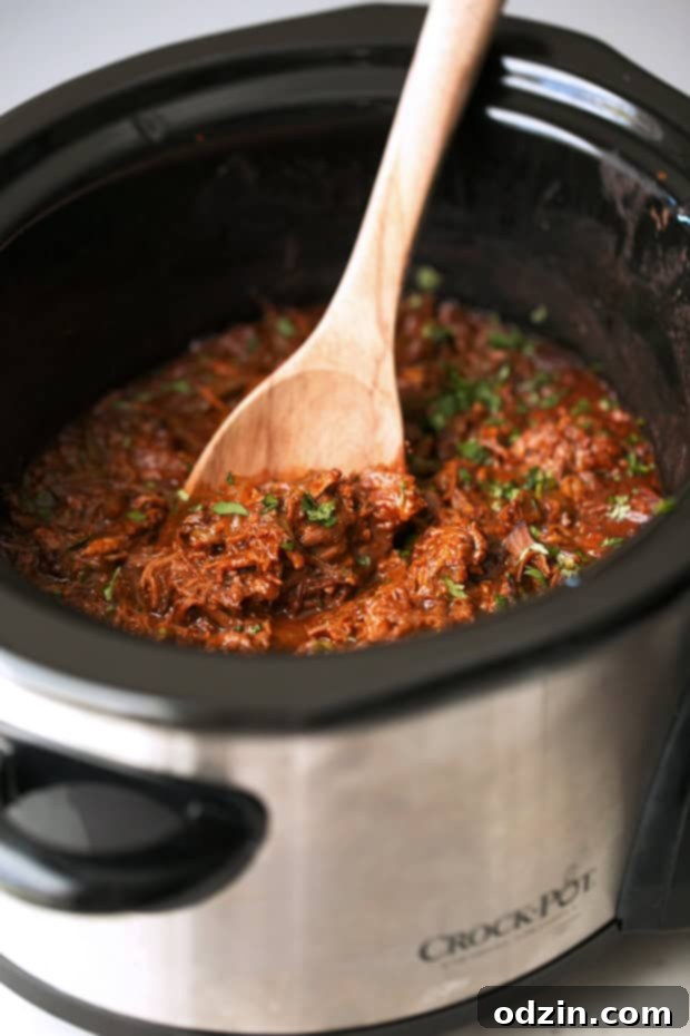 Melt-in-Your-Mouth Cuban Ropa Vieja 4 Slow cooker filled with shredded Ropa Vieja, ready to be served, with a wooden spoon.