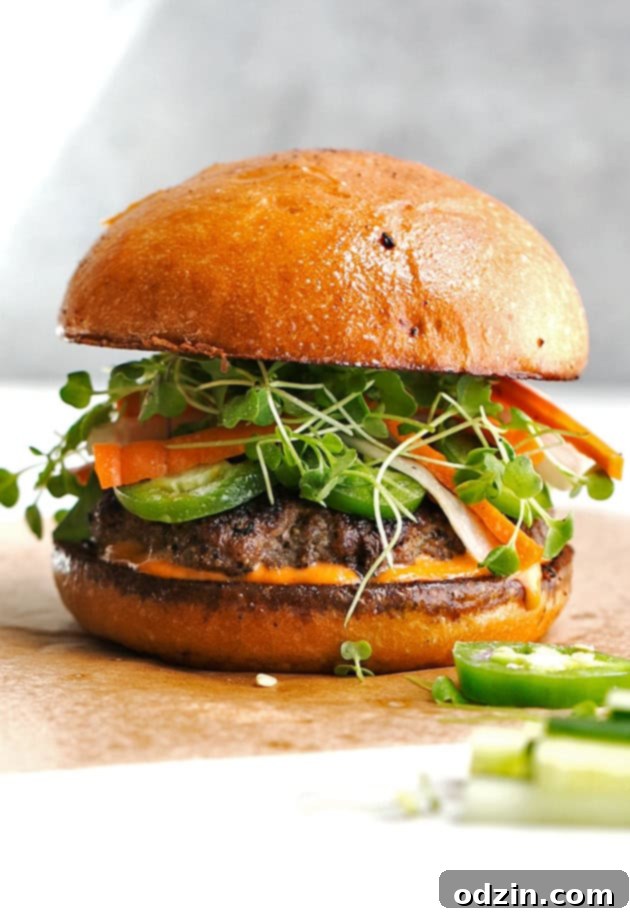 Homemade Banh Mi Burgers with Spicy Sriracha Mayo featuring juicy beef patties, pickled daikon and carrots, fresh cilantro, and sliced jalapeños. Perfect for grilling or skillet cooking! #banhmi #banhmiburger #burgers #pickledveggies #grilling