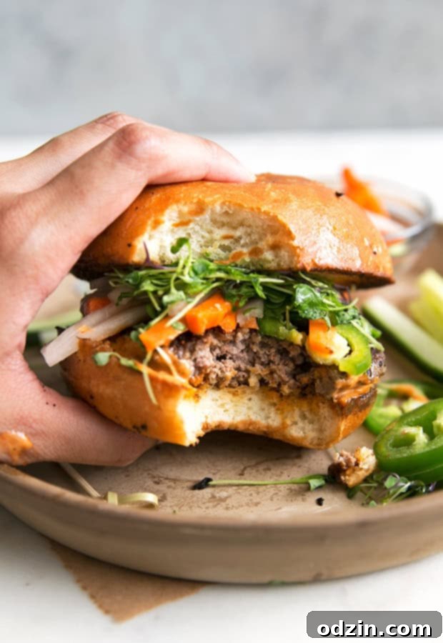 Assembled Banh Mi Burger with a juicy patty, pickled veggies, fresh cilantro, and a generous spread of spicy sriracha mayo on a toasted bun.