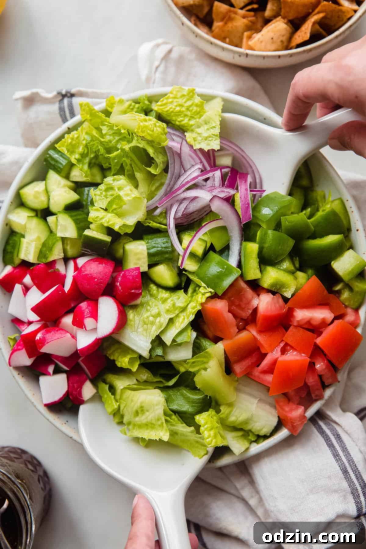 hands tossing fattoush salad in bowl with ceramic salad tongs