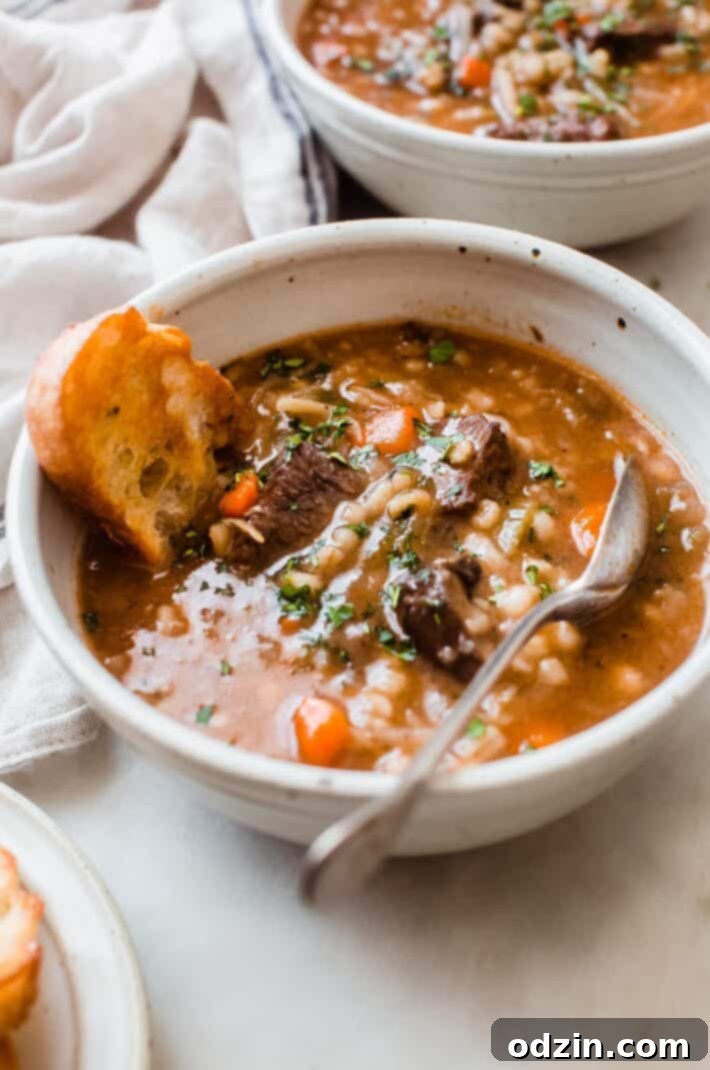 soup filled bowl with spoon and bread on white marble