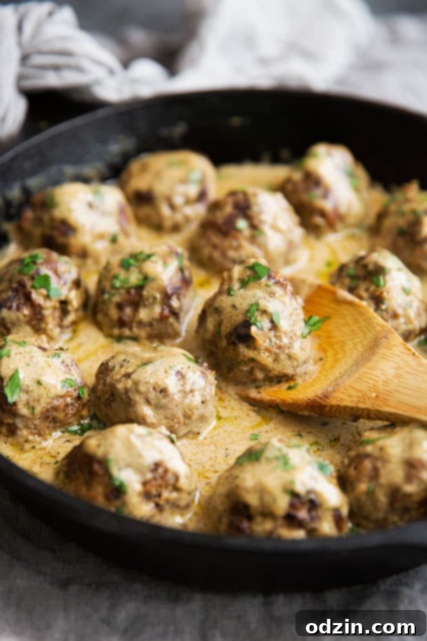wooden spoon lifting sauced meatballs from skillet