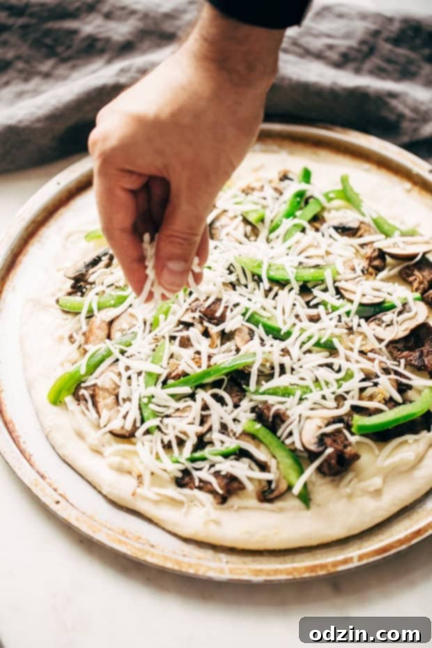 A slice of homemade Philly Cheese Steak Pizza being pulled from the whole pie, showing off the perfectly melted cheese and generous toppings.