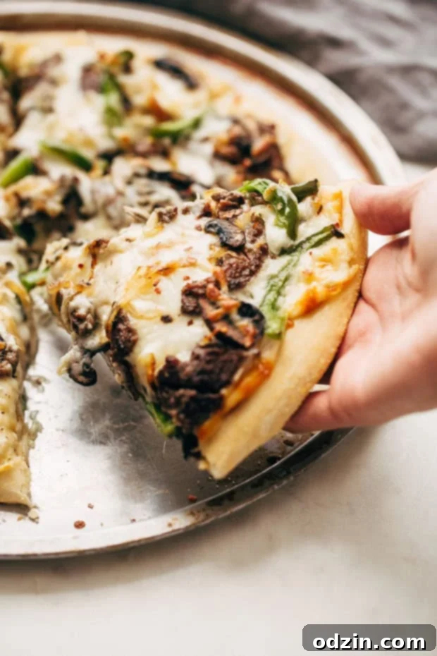 A close-up shot of a baked Philly Cheese Steak Pizza, steam rising, ready to be sliced and enjoyed.