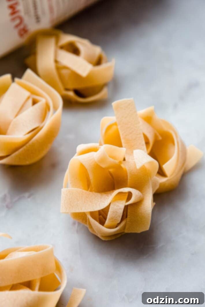 Nests of dried pappardelle pasta arranged on a white marble surface, highlighting their broad, flat shape.