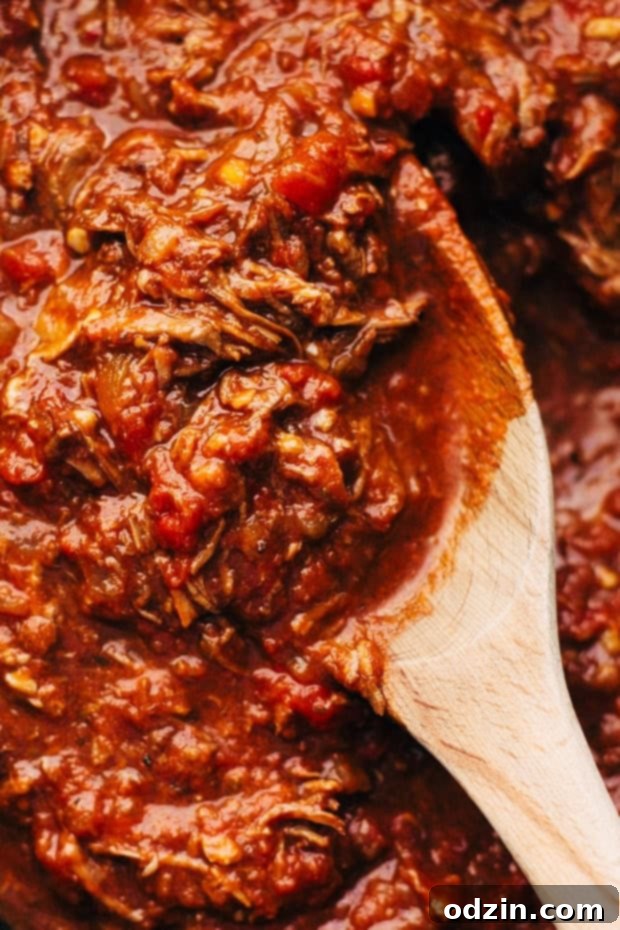 Shredded beef ragu simmering beautifully in a cast iron pot, with a wooden spoon resting inside.