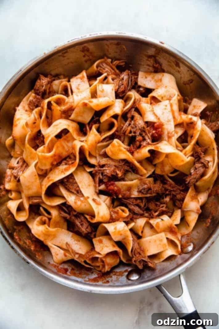 A large skillet brimming with pappardelle pasta expertly tossed in rich beef ragu, ready for serving.
