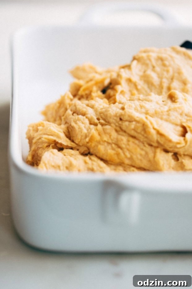A spoon scooping out the soft, cooked flesh from a baked sweet potato into a bowl.