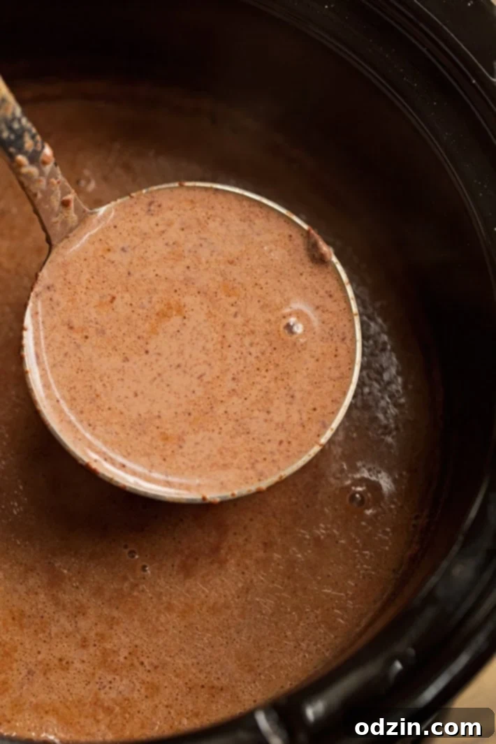 DIY Hot Chocolate Bar Party - Learn how to set up your own hot chocolate bar! Tons of printables, decorating ideas, and toppings! Plus, the most luxurious hot chocolate recipe! #hotchocolate #hotchocolatebar #diyhotchocolatebar #slowcooker | Littlespicejar.com hot chocolate being served from a slow cooker