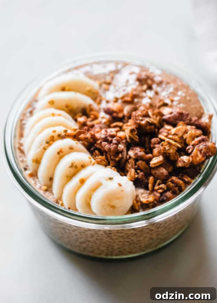 Vibrant orange pumpkin chia seed pudding in a glass bowl, garnished with sliced bananas and a generous sprinkle of golden-brown pumpkin granola, ready for a healthy fall breakfast.