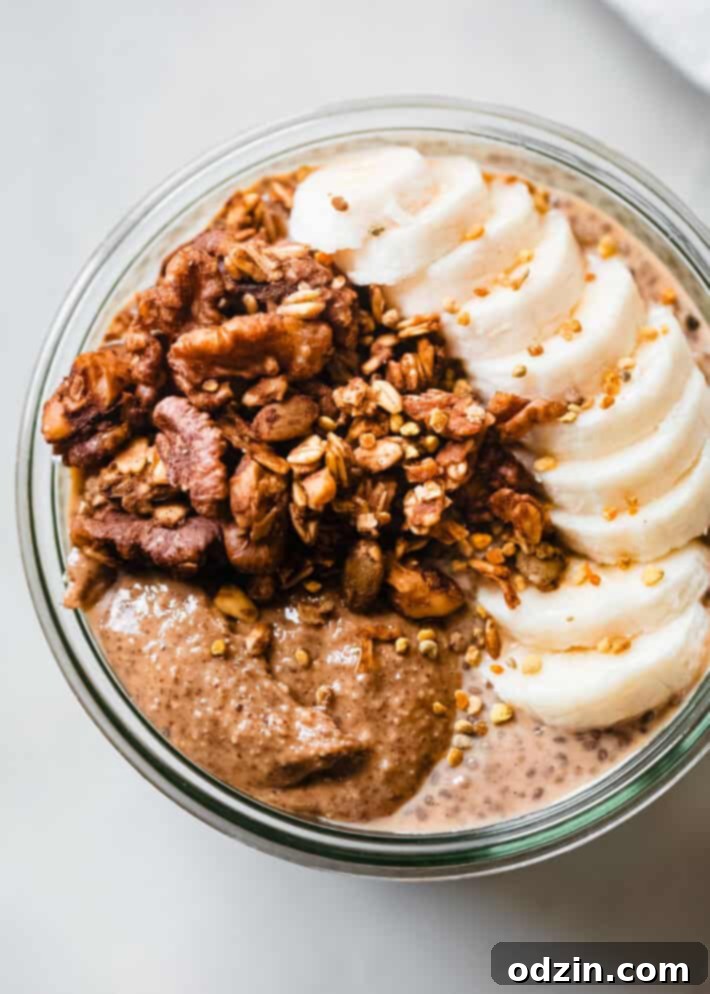 Close-up of creamy pumpkin chia seed pudding, layered with crispy pumpkin granola and fresh banana slices, served in a glass bowl on a rustic wooden surface.