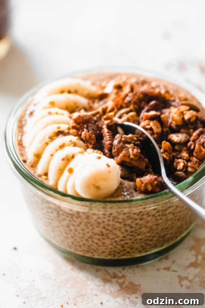 Two glass bowls of pumpkin chia seed pudding, one with a spoon, generously topped with banana slices, granola, and almond butter, ready to be enjoyed.