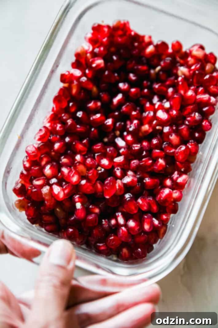 Fresh, vibrant pomegranate arils displayed in a clear glass container, showcasing their beautiful ruby red color and readiness for the holiday salad