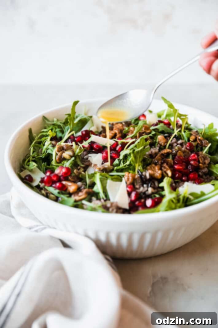 Freshly prepared holiday salad being generously drizzled with homemade orange-shallot vinaigrette dressing in a beautiful white bowl