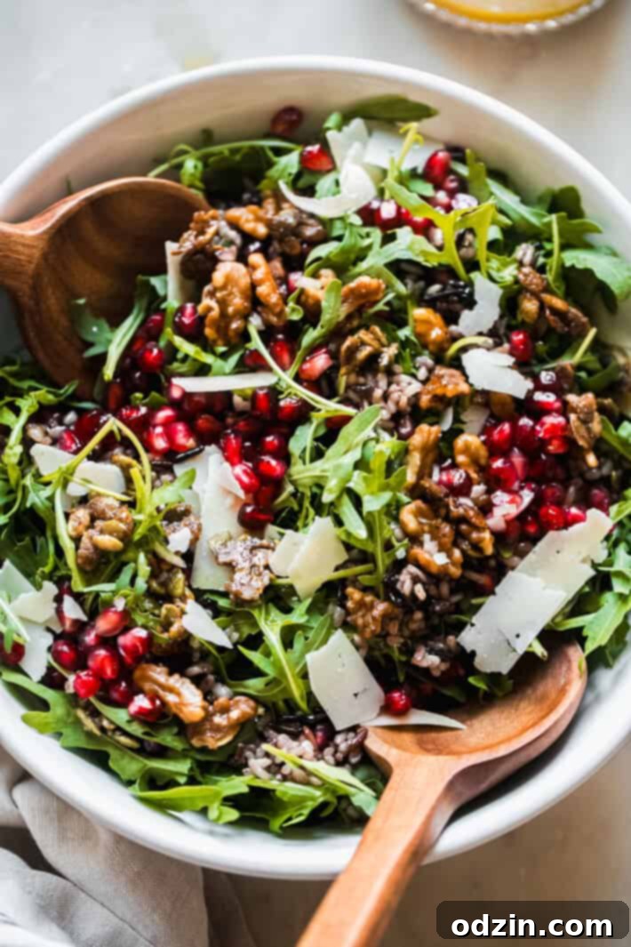 Beautifully presented holiday salad, featuring a vibrant medley of fresh arugula, bright pomegranate arils, crunchy candied walnuts, generous shavings of Parmesan cheese, all lightly coated in a glistening shallot vinaigrette