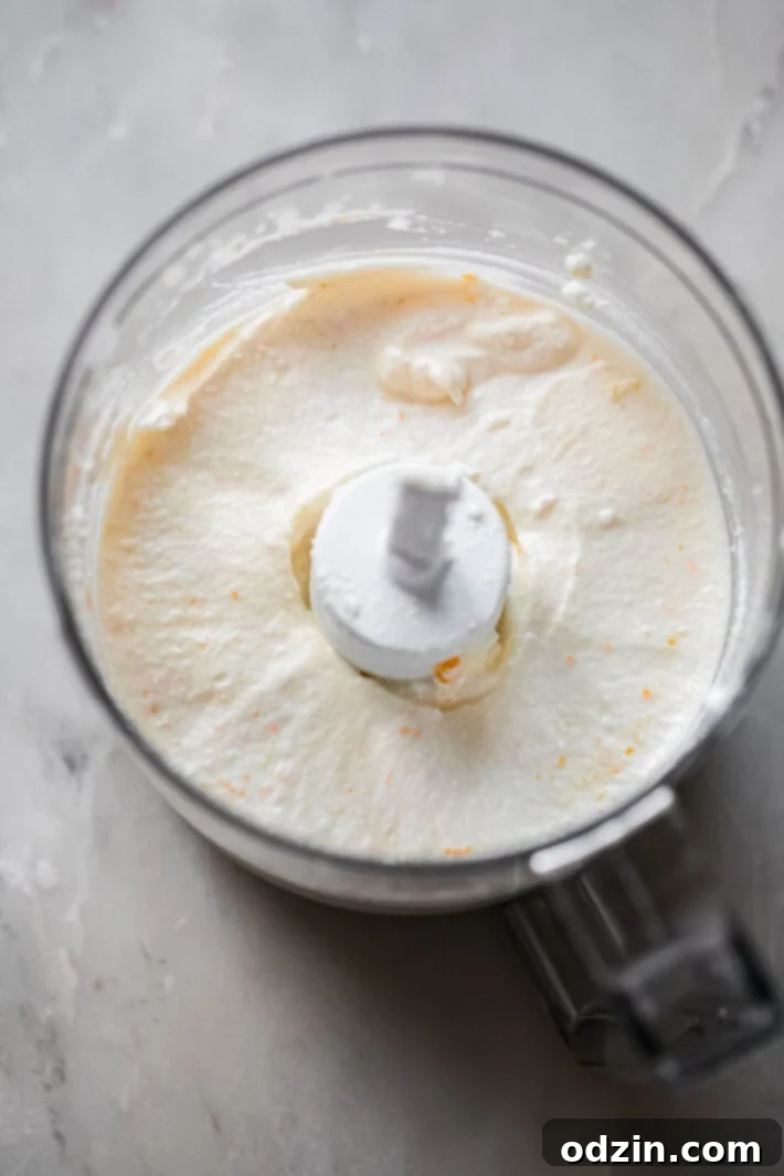 Whipped ricotta in a food processor bowl, showcasing the creamy texture and flecks of orange zest.